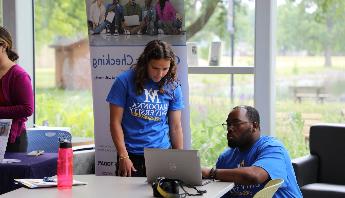 a male 和 a female looking at a computer screen wearing madonna university shirts